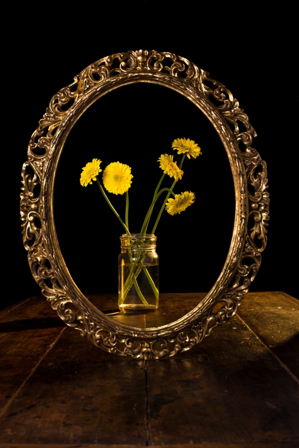 Vertical shot of yellow flowers in a glass jar reflected on the mirror